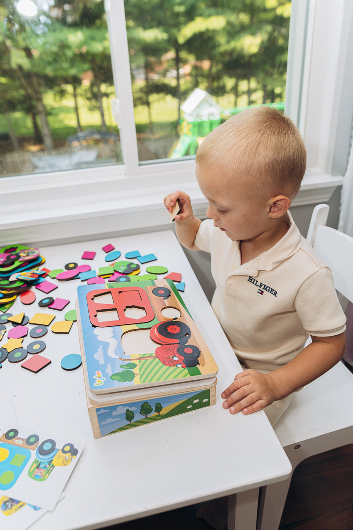 Child playing with colorful puzzle pieces at a table near a window with a view of trees.